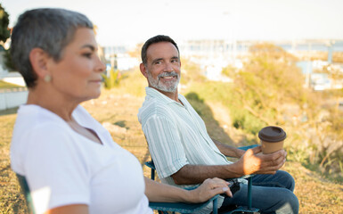 Fototapeta na wymiar Senior man and woman relaxing by ocean enjoying coffee outside