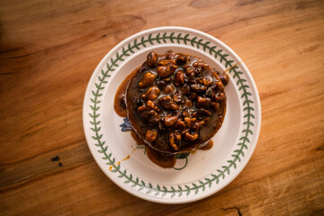 coffee cake with carrot and nuts in a caramel sauce on a white plate and wood table 