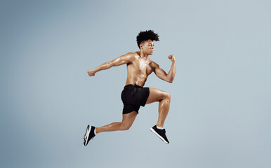 Obraz premium Athletic fit man sprinting and leaping forward on blue background