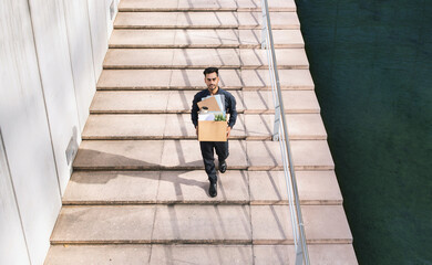 Arabic business guy holding box belongings walking up steps outside