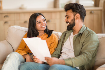 Young Hindu couple discussing papers on sofa at home