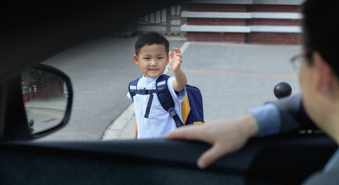 The little boy waved goodbye to his father in the car