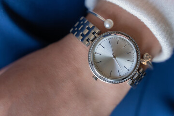 Mechanical women's watch of silver color with rhinestones on a woman's wrist on a blue background