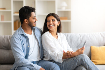 Young loving Indian couple sharing a joyful moment with smartphone at home