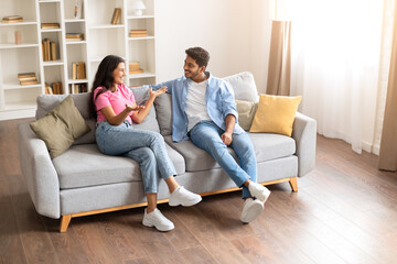 Indian couple chatting animatedly on their living room sofa © Prostock-studio
