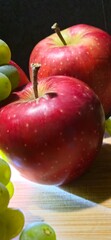 Ripe red apples with green grapes on a wooden board.