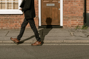 Abstract view of a male Estate Agent seen walking down a terraced English street.  The shadow of...