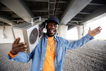 Young excited male hip hop dancer with tape recorder looking at camera while performing dance moves...