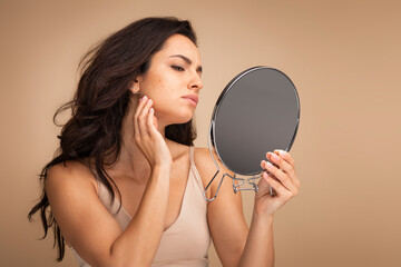 Stressed sad young woman wearing beige top looking at mirror