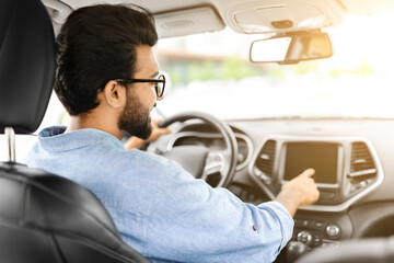 Happy young indian man driving car and listening to music