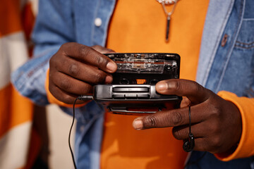 Close-up of young African American man in casualwear putting cassette into old walkman with...