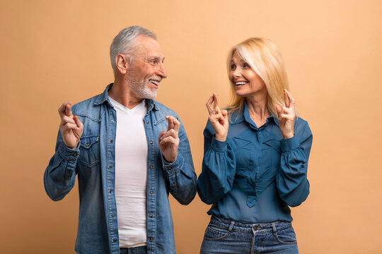 Happy senior man and woman crossing fingers, beige background