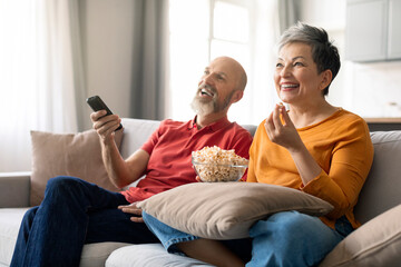 Domestic Leisure. Happy Senior Spouses Watching Tv At Home And Laughing