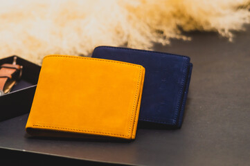 New wallet made of high quality leather. Brown and blue stacked together leaning on a black box Background with yellow dry grass and black background. Studio shot.