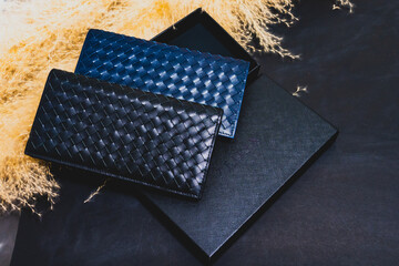 High-quality genuine leather wallets, available in two colors, stacked on top of a black packaging box. On a black background over golden dried flowers. Studio shot. Promotional photo.
