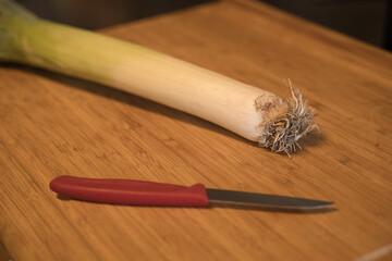 a stick of leek with a knife on a wooden board