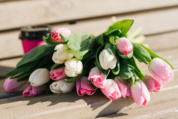Bouquet of pink and white tulips and a paper cup of takeaway coffee on a bench