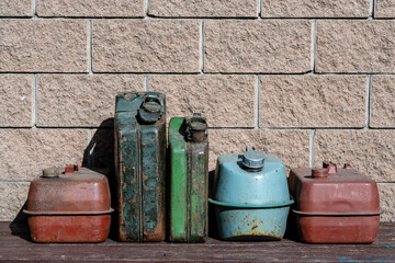 Many old rusty iron fuel cans on a table near the garage, closeup. Various metal painted canisters for gasoline, retro style