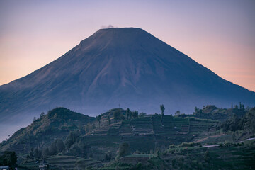 Telephoto of peak of Sindoro Mountain with hills in sunrise time. Dieng Regency, Indonesia