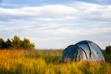 A tourist tent stands on a large clearing on a summer day - obrazy, fototapety, plakaty