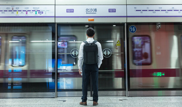 The back of a middle-aged man waiting for a bus in a subway platform