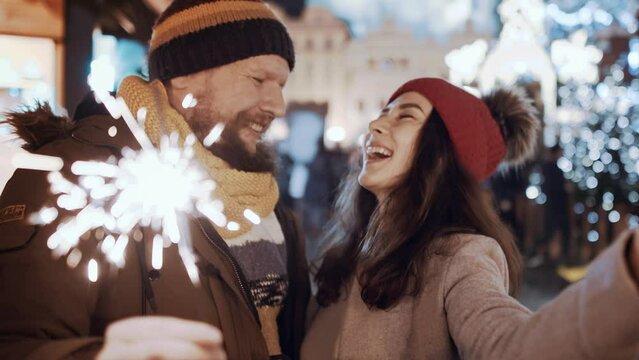Multiracial couple have fun kiss with sparklers outdoor celebrating merry Christmas xmas and happy new year. Young man woman on date smiling waving firework express joy happiness. Christmas holiday