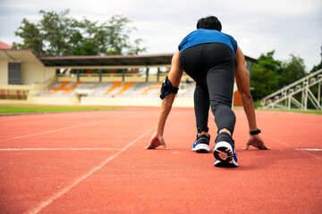 Asia male teenager getting ready starting to run on track in stadium, backshot view low angle