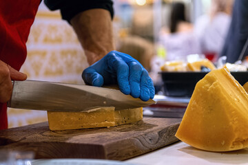 Seller slicing cheese on wooden board. Cheese shop.