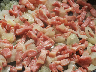 Close view of a saut&eacute; of lardons and onions in a pan, while they are cooked