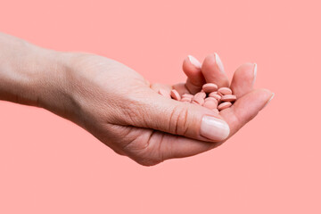 Close-up of many pink pills in woman hand on pink background. Medical concept of medicine treatment, vitamins, supplements, contraceptive pills or feminine drug addiction. Selective focus