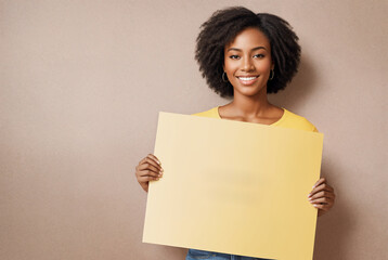 Black woman holding white sign paper in her hands and smiling at the camera with yellow background.Minimalism.Creative designer fashion glamour art.