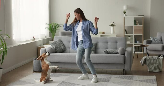 Happy excited beagle owner woman dancing at home with adorable barking spinning trick dog, enjoying home activity, leisure time with cute beloved pet, smiling, laughing, having fun