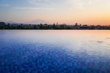 Fototapeta na wymiar Blue swimming pool in hotel rooftop with beautiful mountain and rice paddy fields view in the morning. Swimming pool and relaxing area in the apartment. Concept for summer holiday.
