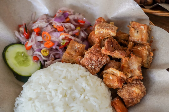 Crispy fried pork served with white rice, sambal matah and sliced cucumber. Balinese mixed rice or nasi campur. Bali authentic delicious food. Concept for bali tourism and culinary.