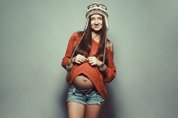 Stylish pregnancy concept. Portrait of happy hipster mommy with hands on stomach posing in trendy...