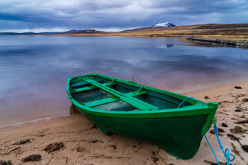 Green rowing boat tied up by a remote mountain lake