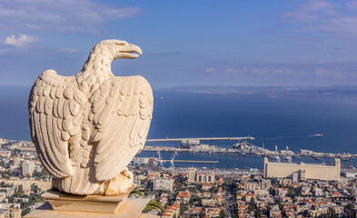 The statue of eagle on the fence at Bahai garden with the view on the Israeli city of Haifa, port,...