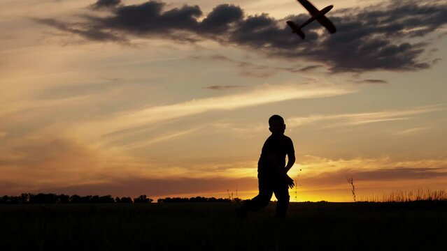 Boy running with plane in park, Silhouette. Happy kid runs with toy airplane against background of summer nature in field at sunset. Leader of Happy baby an outdoor winner. Childs dream flight Concept