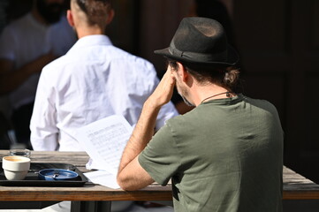 A thoughtful older man wears a traditional hunting hat while he looks at a businessman in front of...