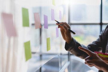Team business people writing planning and brainstorming putting sticky notes on glass wall in the...