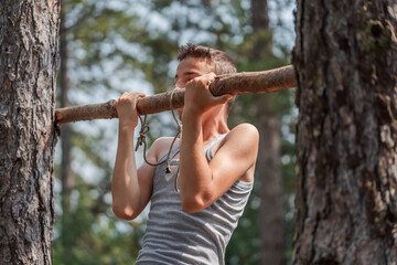 Portrait of concentrated boy in T-shirt doing pull ups on horizontal bar outdoors. Healthy lifestyle concept. Blurred background. High quality photo