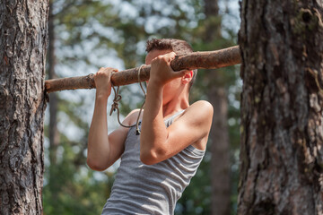 Portrait of concentrated boy in T-shirt doing pull ups on horizontal bar outdoors. Healthy lifestyle concept. Blurred background. High quality photo