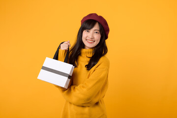 Young Asian woman in her 30s, carrying a shopping paper bag, wearing a yellow sweater and red beret, enjoying a successful shopping day against a yellow background.