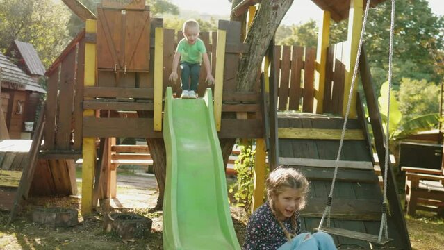 Young kids playing in treehouse going down the slide