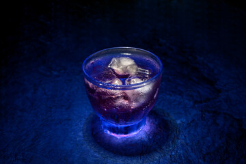 A transparent glass in the neon lights on the table background. Cocktail, party, and night life concept.