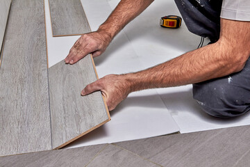 Installing laminate floor, detail on man hands holding wooden tile, over white foam base layer