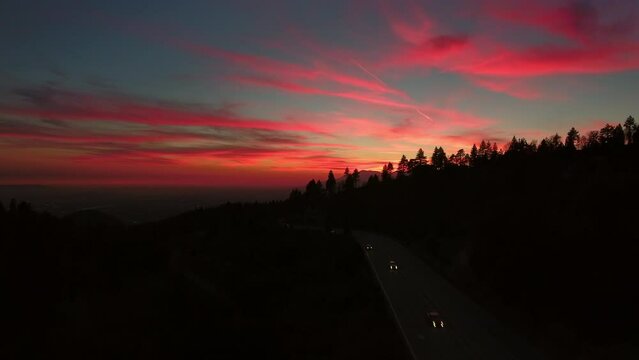 Aerial Ascending Shot Of Vehicles On Mountain Road Amidst Silhouette Trees Against Sky At Sunset - Big Bear Lake, California