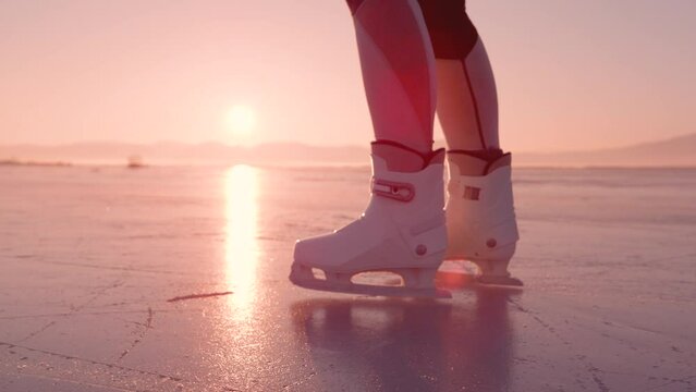 SUPER SLOW MOTION, CLOSE UP: Female skating on glittering surface of a frozen lake in golden sunset light. She is sliding on naturally frozen ice with her white skates on a beautiful sunny winter day.