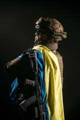 Rear view of a brave young soldier with modern weapons and the Ukrainian flag on his shoulder. A military man in a helmet looks to the side in the smoke.