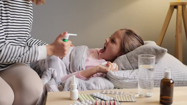 Unwell childcare. Comfortable recovery. Medical healthcare. Ill little girl has fever lying in bed her mother taking care and touch to feel body temperature treating sore throat with spray.